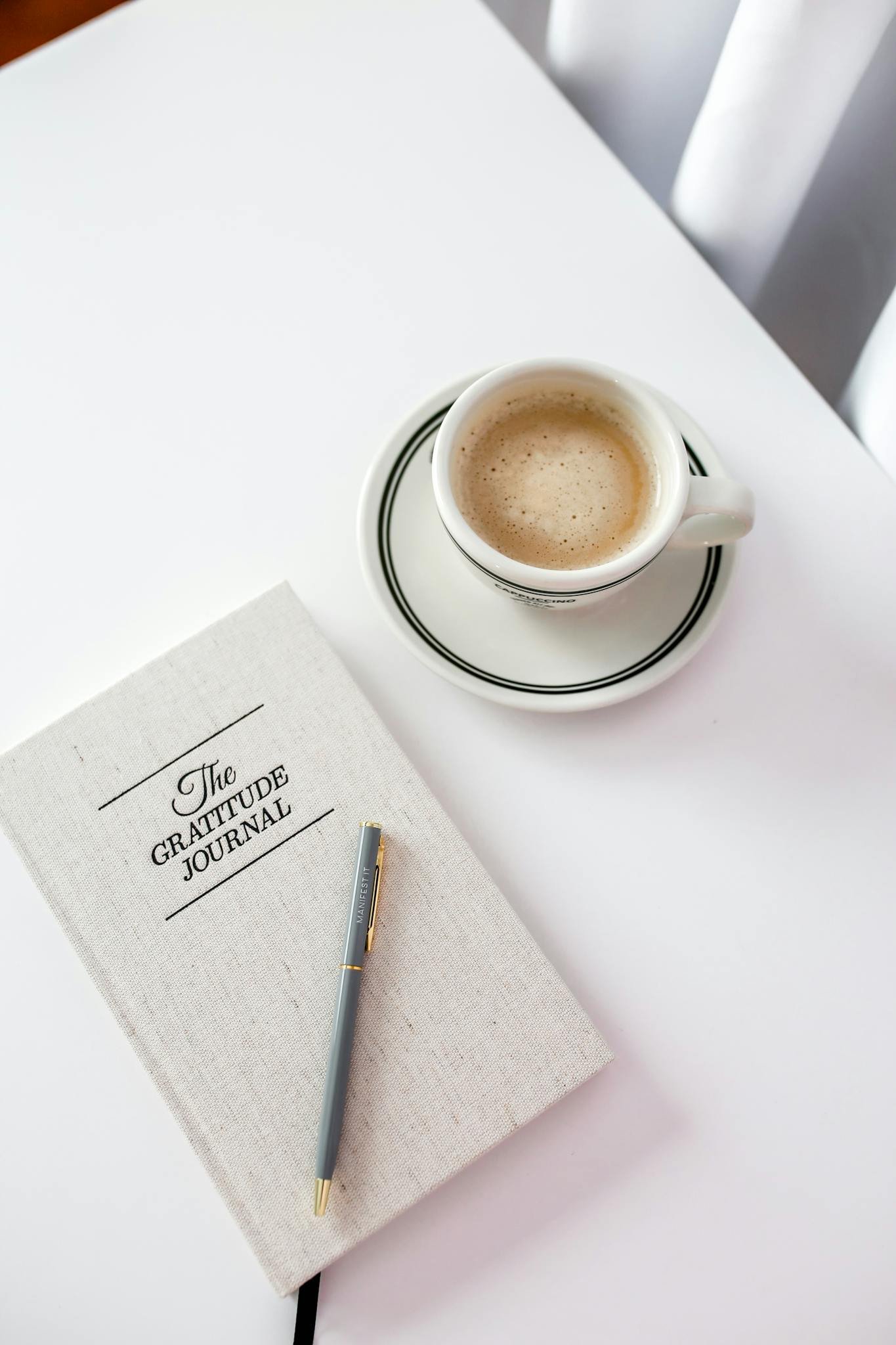 A gratitude journal beside a cup of coffee on a bright, minimalist table setting.