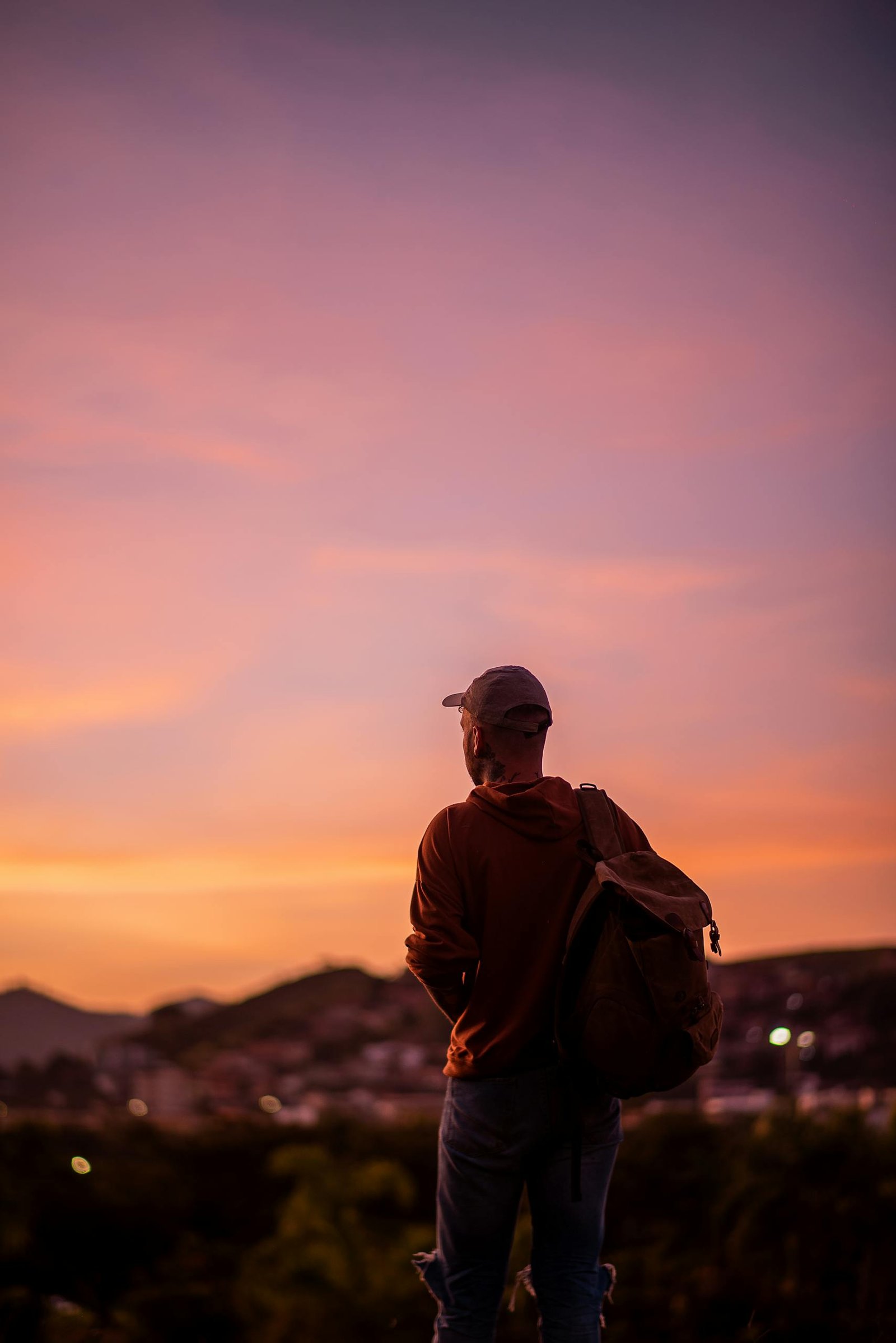 A person with a backpack stands against a vibrant sunset in Brazil.