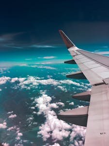 Aerial view of an airplane wing traveling over fluffy clouds with a deep turquoise sky.