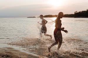 Two teenagers running on a beach at sunset, enjoying the summer seaside with splashes.